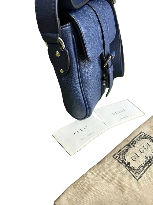 Blue Gucci handbag on a green cloth with two cards and a logo print.