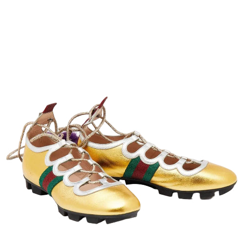 A pair of metallic gold leather athletic shoes with white and green web stripe details, beige laces, and black soles, photographed on a light gray background.