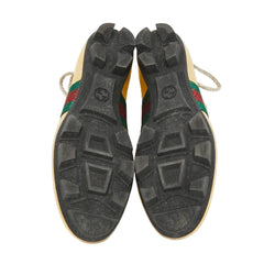 The soles of a pair of Gucci sneakers, showing the black treaded rubber and the iconic green and red web stripe on the sides, photographed from above on a white background.