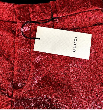 Close-up of red Gucci trousers with a textured metallic finish, featuring a white Gucci hangtag attached at the waistband.