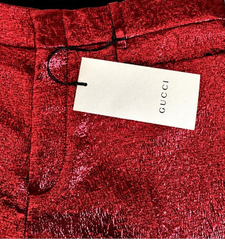 Close-up of red Gucci trousers with a textured metallic finish, featuring a white Gucci hangtag attached at the waistband.