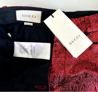 Close-up of a Gucci garment interior and attached white Gucci tags, showing a black lining, red textured fabric, and Gucci labels.