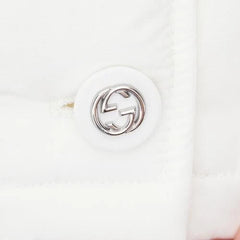 Close-up of a white handbag with a silver logo on a light pink background