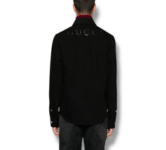 A man viewed from the back wearing a black Gucci shirt jacket with silver rhinestone lettering across the upper back, paired with dark trousers.