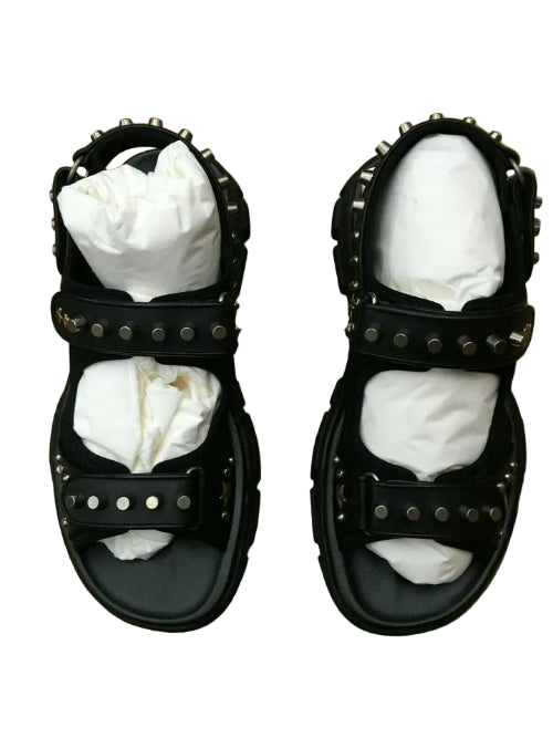 Black studded sandals with white socks on a patterned surface