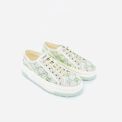 A pair of Gucci low-top sneakers featuring a light beige canvas upper with a green GG monogram pattern, cream laces, and a thick white platform sole with a pale mint green edge, set against a plain light gray background.