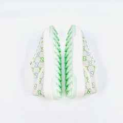 A pair of low-top sneakers shown from the side, featuring a white canvas upper with a green and gray monogram pattern, white laces, and a chunky white sole with a mint green textured zigzag design on the outsole.