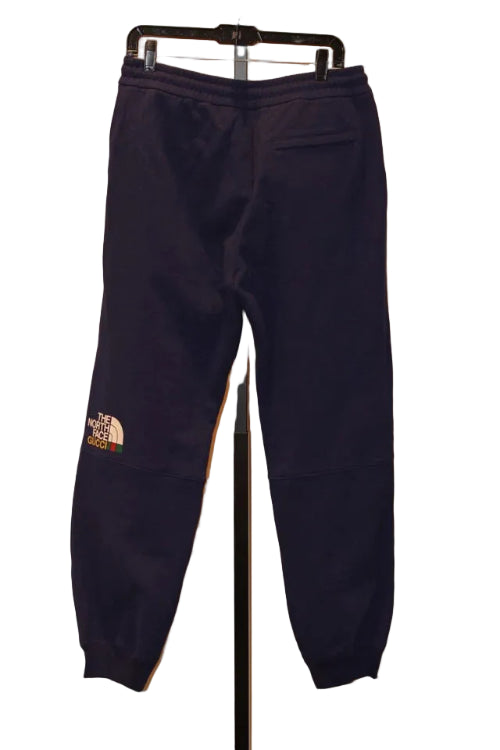 Navy blue sweatpants with a brand logo on a hanger against a neutral wall.
