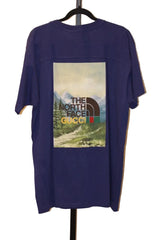 Purple t-shirt with 'The North Face' and 'Gucci' logos on a hanger against a white wall.