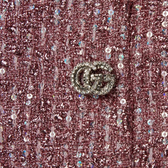 Close-up of a pink glittery fabric with a decorative button featuring a logo.
