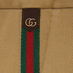 Close-up of a beige woven textile with a vertical green and red stripe and a brown rectangular patch featuring a gold interlocking GG logo.
