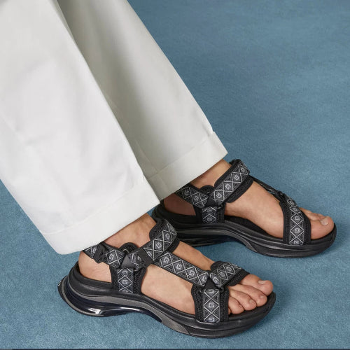 Black sandals worn with white pants on a blue background