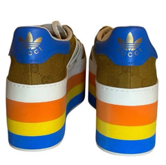 A pair of low-top sneakers shown from the back, featuring a multicolor design with blue, gold, brown, orange, yellow, and white stripes on the stacked heel and white midsoles.