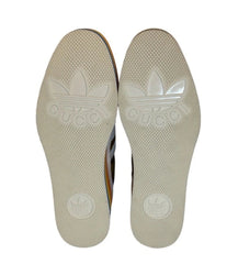 A pair of beige slip-on shoes with a circular logo printed on the sole, shown against a plain white background.