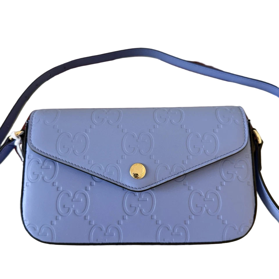 Blue Gucci handbag on a wooden surface with Gucci logo in the background