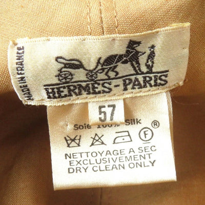 Close-up of a Hermès Paris garment label sewn onto tan fabric, showing the black horse-and-carriage logo and care instructions for dry cleaning.