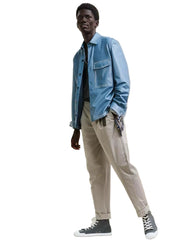 Person wearing a blue denim jacket, beige pants, and black sneakers on a white background