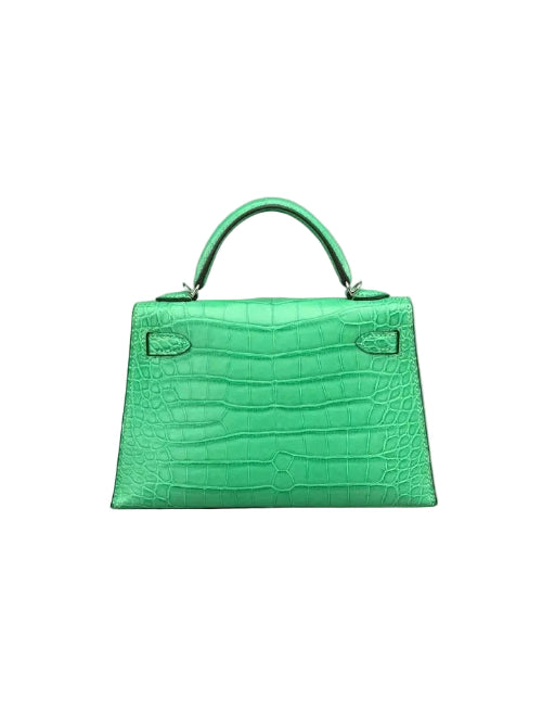A bright green crocodile-embossed leather handbag with a top handle, photographed against a neutral gray background.