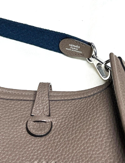 Close-up of a gray handbag with a blue strap and Hermes logo.