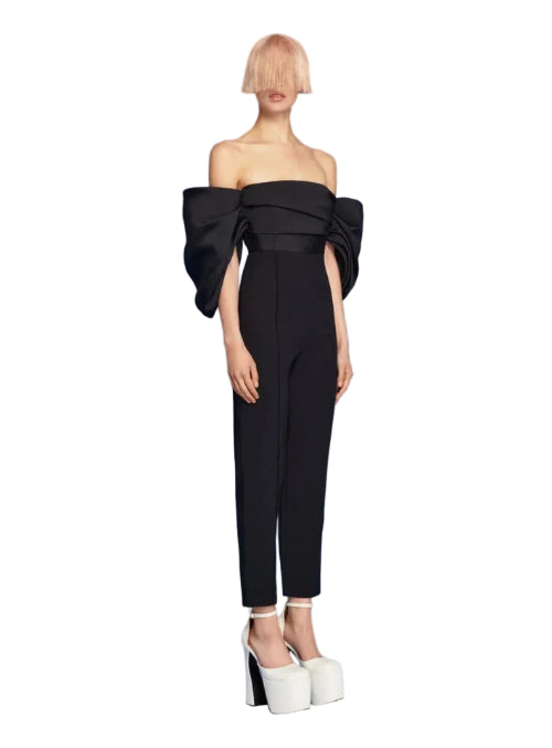 Woman wearing a black off-shoulder jumpsuit on a blue background