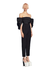 Woman wearing a black off-shoulder jumpsuit on a blue background