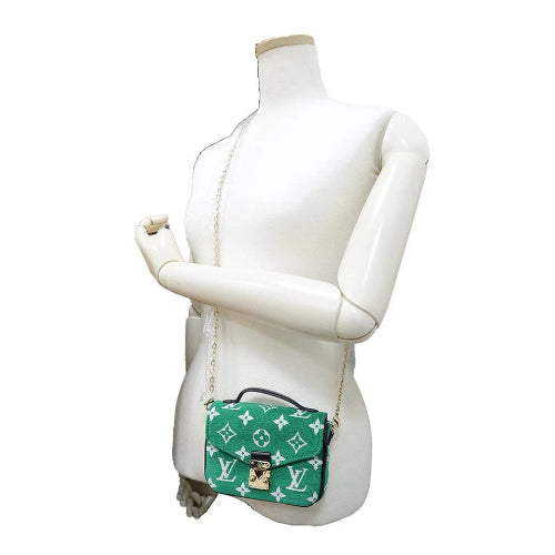 Green handbag with white monogram pattern on a mannequin against a white background