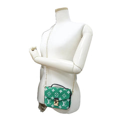 Green handbag with white monogram pattern on a mannequin against a white background