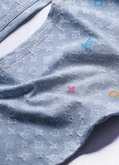 A close-up of a light blue denim garment featuring an all-over embossed Louis Vuitton monogram pattern and small embroidered LV logos in blue, pink, and yellow.