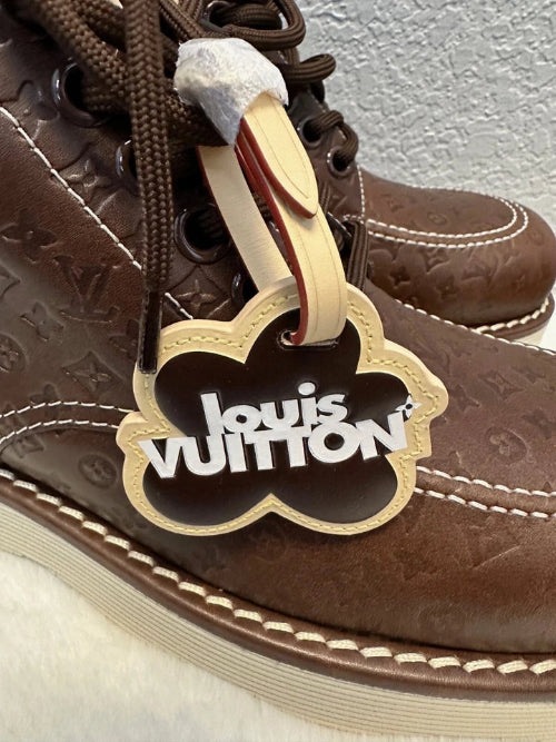 A close-up of a brown leather Louis Vuitton shoe with a white and gold paper tag attached to the side, showing the brand name 'Louis Vuitton' in gold lettering.