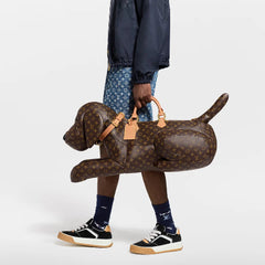 A person wearing dark pants and patterned socks holds a brown plush dog toy against a plain white background.