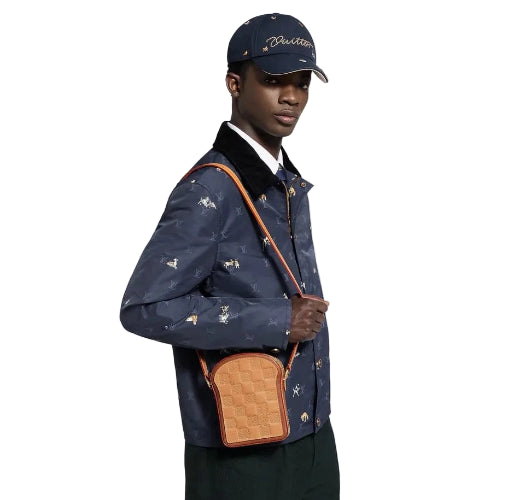 Person wearing a patterned jacket and cap, holding a brown leather bag against a white background