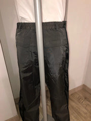 Person wearing dark pants and a white shirt standing against a plain background