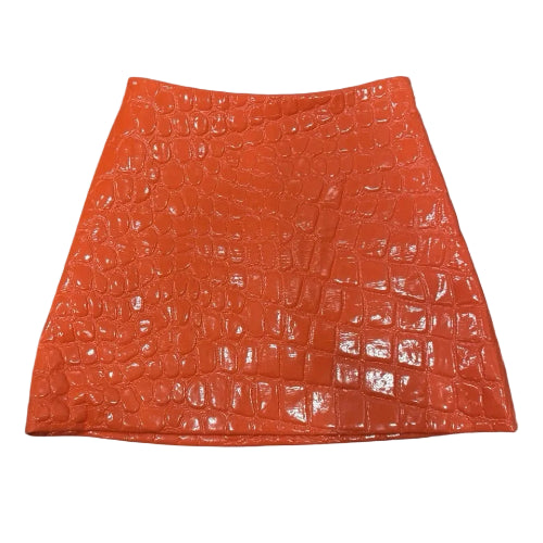 A bright orange textured skirt with a crocodile-embossed pattern, shown flat against a blue sky background with white clouds.
