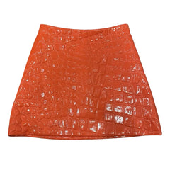 A bright orange textured skirt with a crocodile-embossed pattern, shown flat against a blue sky background with white clouds.