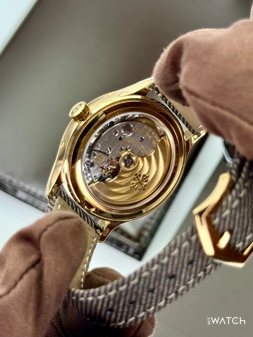 Gold watch with visible mechanical components held by a person wearing brown gloves.