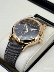 Luxury watch with gold case and dark strap on a white cushion