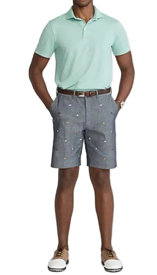 Man wearing a light green polo shirt and gray shorts with a pattern on a white background