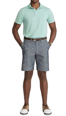 Man wearing a light green polo shirt and gray shorts with a pattern on a white background