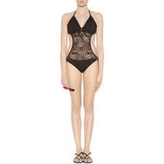 A model wearing a black lace halter neck one-piece swimsuit with a deep V-neckline and cutout details, paired with black strappy sandals against a plain white background.