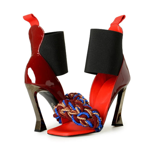 Red high-heeled shoes with black ankle cuffs and braided multicolor heel on a white background