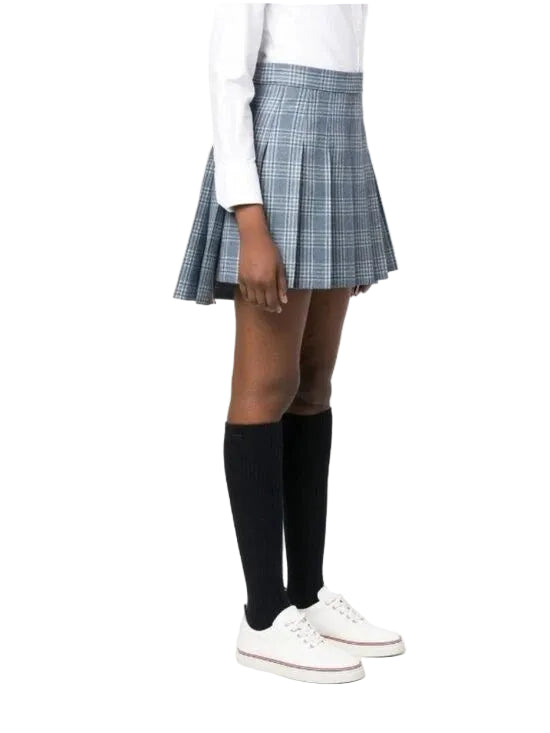 A person wearing a gray and white plaid pleated mini skirt, black knee-high socks, and white sneakers, shown from the waist down against a plain light background.