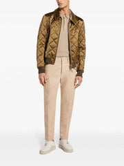 Man wearing a quilted jacket, beige shirt, and pants on a white background