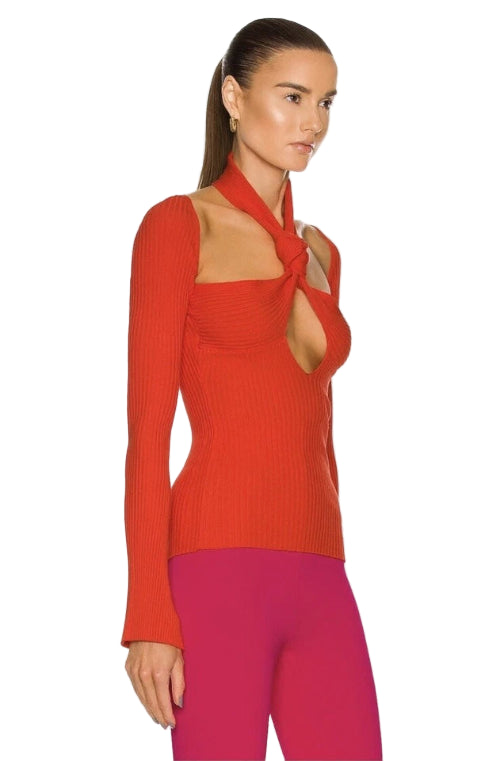 Woman wearing a red ribbed top with a tie detail and pink pants on a white background