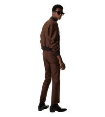A man wearing a brown tailored jacket and matching trousers with black boots and sunglasses, photographed in profile against a clean white studio background.