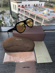 Tom Ford sunglasses with case and box on a reflective surface with a cityscape background