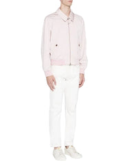 A model wearing a light pink zip-up jacket with a pointed collar, paired with white trousers and white sneakers, shot against a plain light gray studio background.