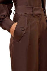 Close-up of a person wearing dark brown wide-leg trousers with a matching waist belt and a side button pocket, paired with a dark long-sleeve top.
