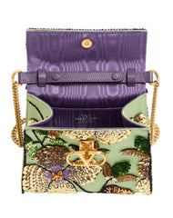 A purple textured leather clutch bag with a gold-tone chain strap and a floral embroidered front pocket featuring green, yellow, and orange details.
