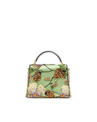 A structured light green handbag with an intricate floral and botanical beaded design in gold, brown, and cream, featuring a dark purple top handle.