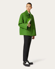 Person wearing a bright green coat and black pants on a white background
